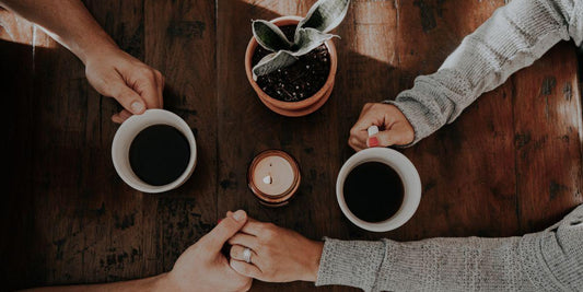 Handen met koffiekopjes en plant op houten tafel, gezellige sfeer voor spelletjesavond