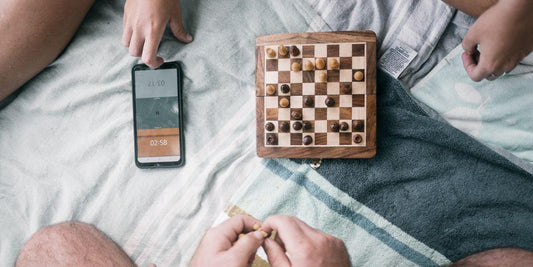 Houten schaakspel met stukken op dekbed, tijd met stopwatch op telefoon, gezellig spel voor jong en oud