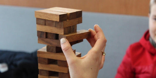 Hand plaatst houten blok bij strategiepuzzelspel, geschikt voor jong en oud